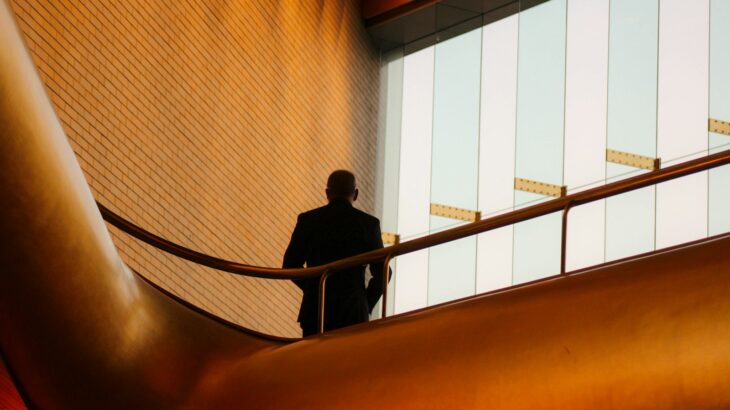 A person in a dark suit on a balcony with a curved gold railing